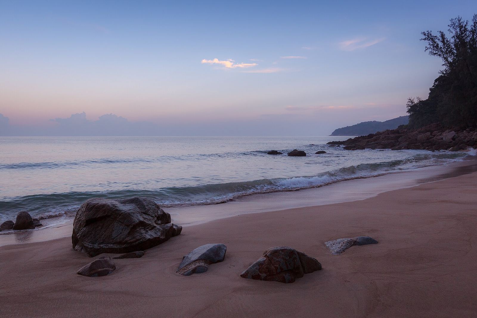 A quiet Phuket beach at dusk with granite rocks and calm water