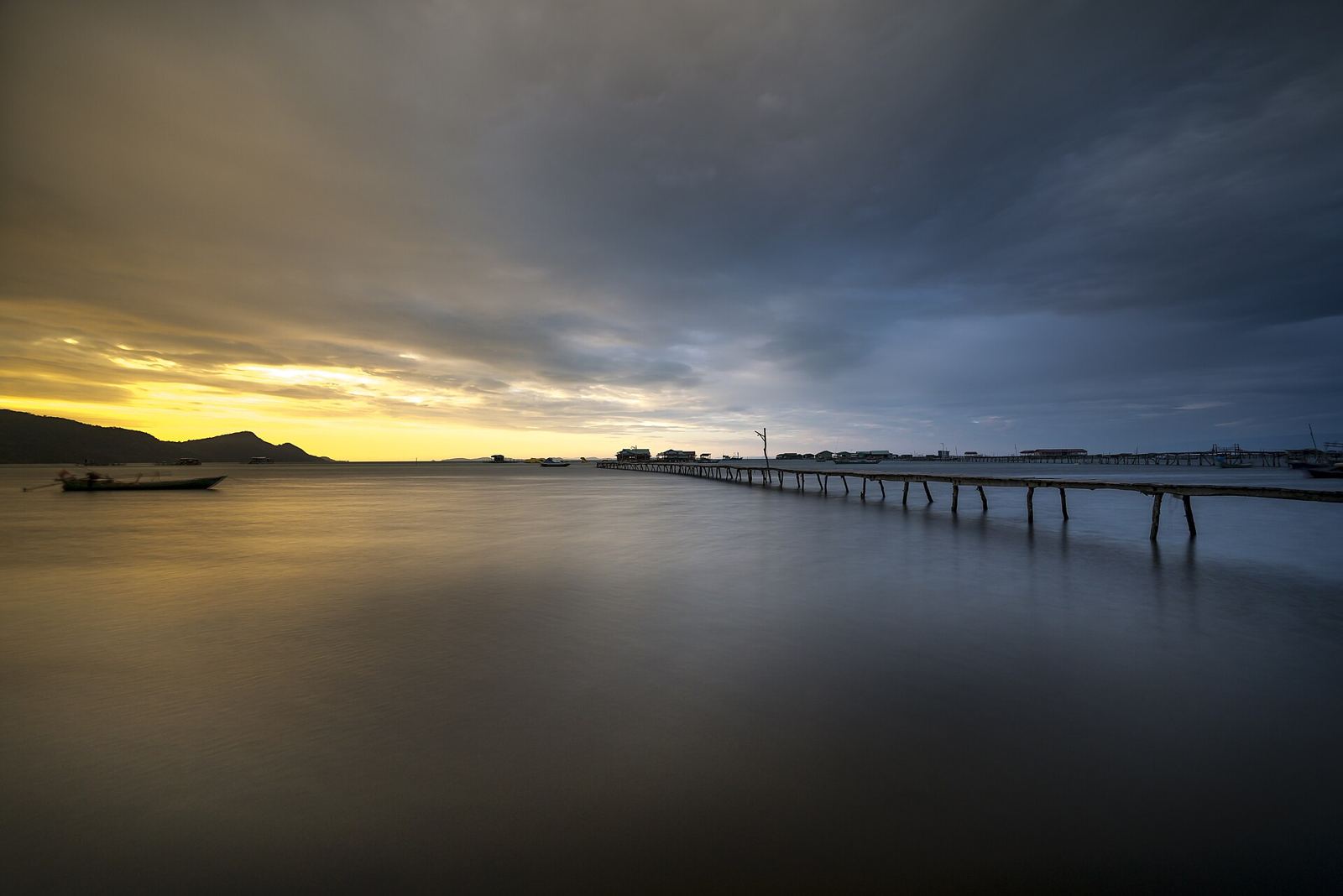 A long wooden pier on Phu Quoc at sunset, with still water and a fishing boat